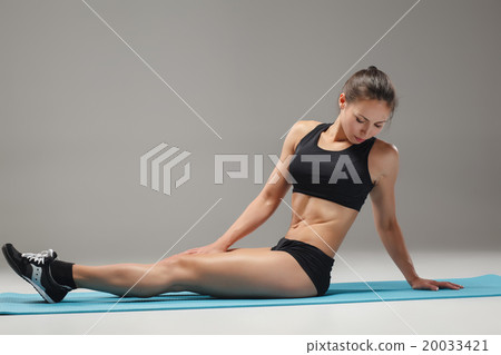 Muscular young woman athlete stretching on gray  20033421