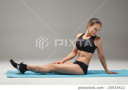 Muscular young woman athlete stretching on gray  20033422
