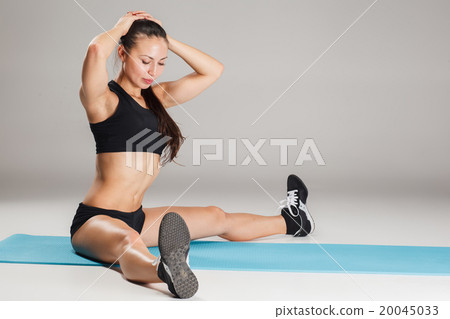 Muscular young woman athlete stretching on gray  20045033