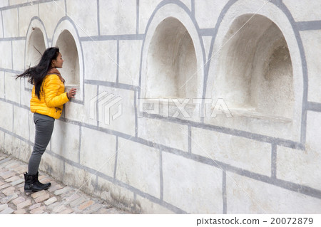Young woman looking out the window in the wall 20072879