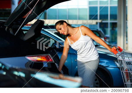 Woman shifts the purchase from shopping cart in the trunk of a c 20090798
