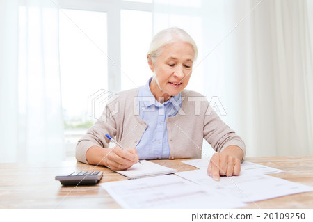 senior woman with papers and calculator at home senior woman with papers and calculator at home 20109250