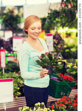 happy woman with shopping basket choosing flowers 20109770