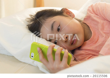 一個女孩在床上看一部智能手機 一個女孩在床上看一部智能手機 20115506