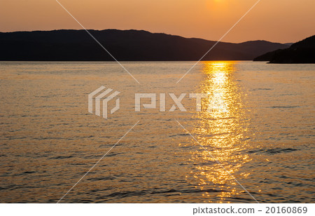 Silhouette of hills by water reflecting sunset 20160869