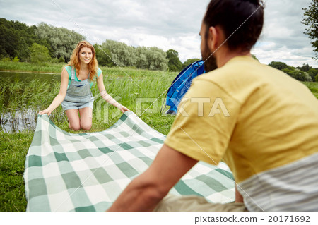 happy couple laying picnic blanket at campsite happy couple laying picnic blanket at campsite 20171692