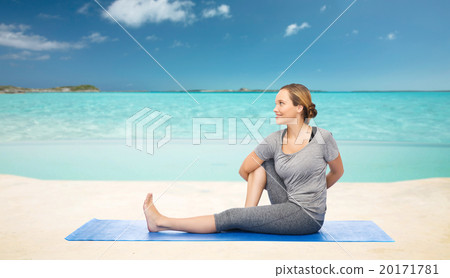 woman making yoga in twist pose on mat over beach 20171781