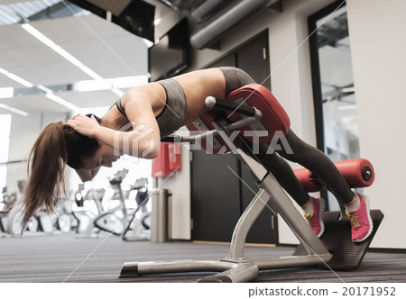 young woman flexing back muscles on bench in gym 20171952