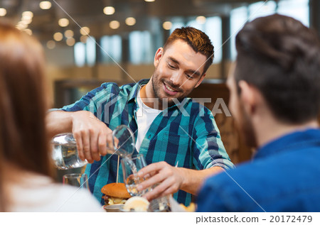 happy man with friends pouring water at restaurant happy man with friends pouring water at restaurant 20172479