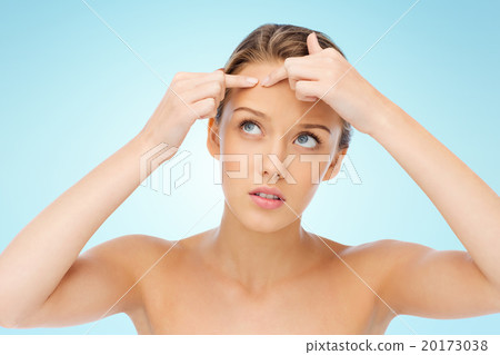 young woman squeezing pimple on her face 20173038