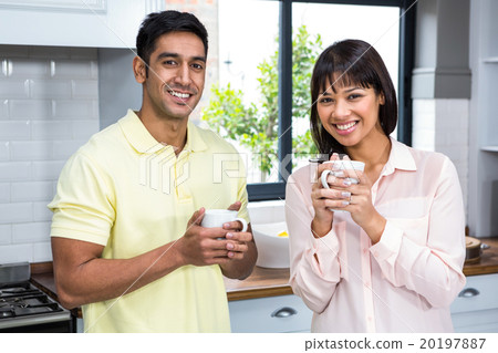 Happy couple smiling at the camera while holding cups 20197887