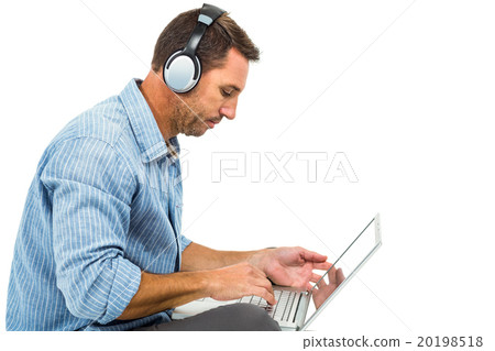Young man sitting on floor using laptop and headphones 20198518