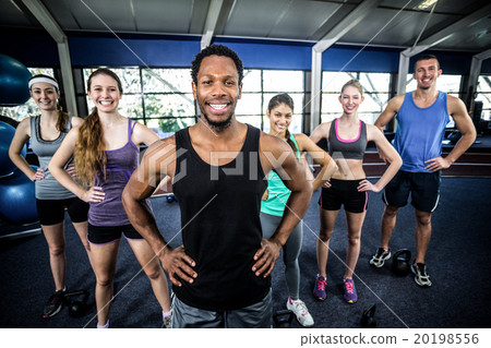 Smiling fitness class posing together with hands on hips Smiling fitness class posing together with hands on hips 20198556