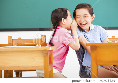 happy little girls whispering and sharing a secret in classroom happy little girls whispering and sharing a secret in classroom 20201185