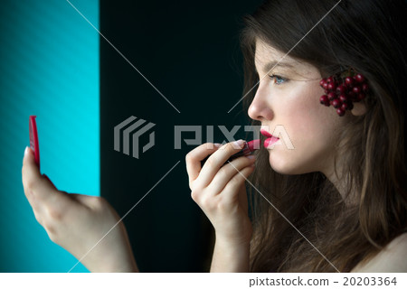 Beautiful young woman putting on lipstick 20203364