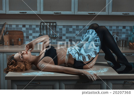 On the kitchen table lies a woman in an apron. 20207368