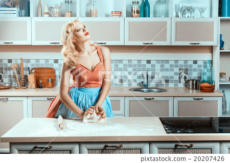 Blonde girl on kitchen kneads dough. 20207426