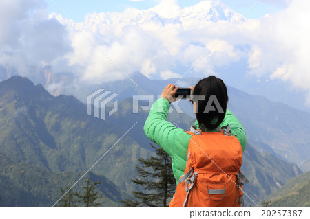 young asian woman backpacker taking photo with smartphone on mountain peak young asian woman backpacker taking photo with smartphone on mountain peak 20257387