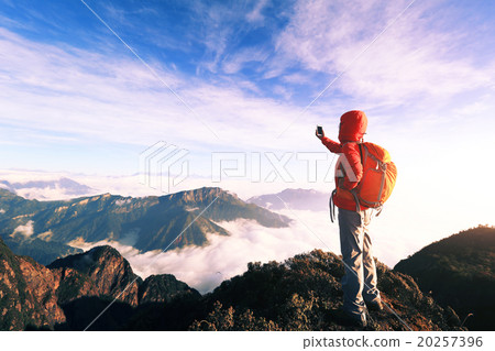 young asian woman backpacker taking photo with smartphone on mountain peak young asian woman backpacker taking photo with smartphone on mountain peak 20257396
