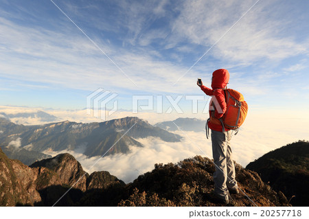 young asian woman backpacker taking photo with smartphone on mountain peak young asian woman backpacker taking photo with smartphone on mountain peak 20257718