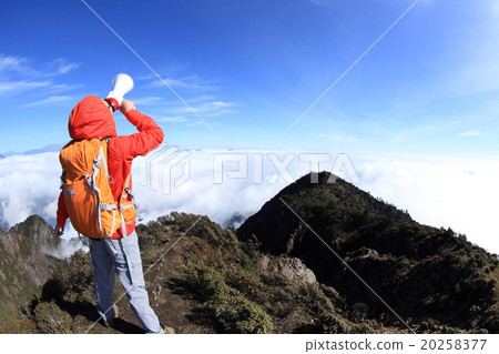 young woman backpacker shouting with loudspeaker on beautiful mountain peak 20258377