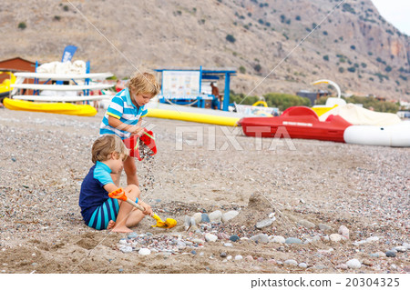 Two little kid boys playing on beach with stones 20304325