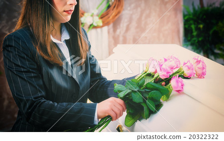 Woman putting rose on coffin at funeral 20322322