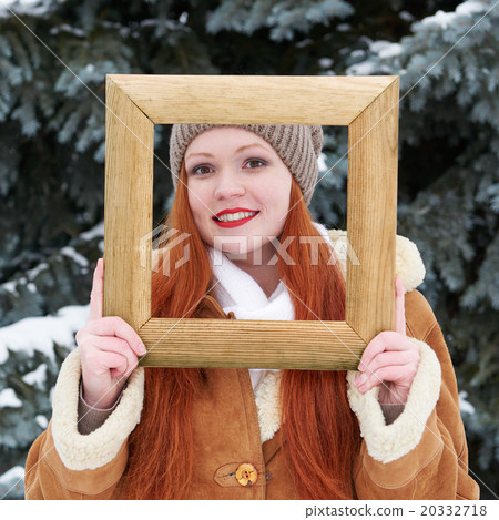 Woman outdoor portrait in wooden photo frame at winter . Snowy weather in fir tree park. 20332718