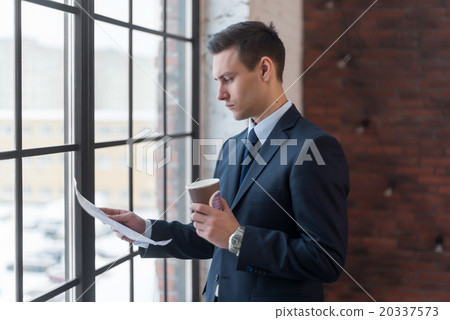 Businessman standing in office reading documents 20337573