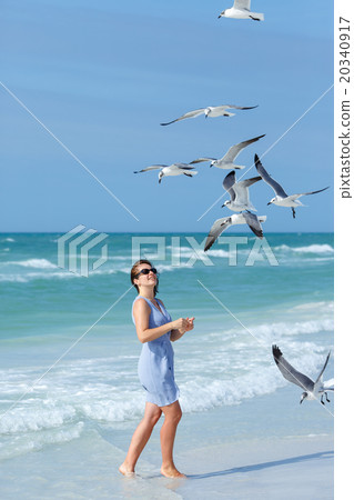 Young woman feeding seagulls on tropical beach 20340917