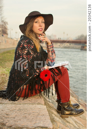 Brunette girl with a book by the river bank 20342136