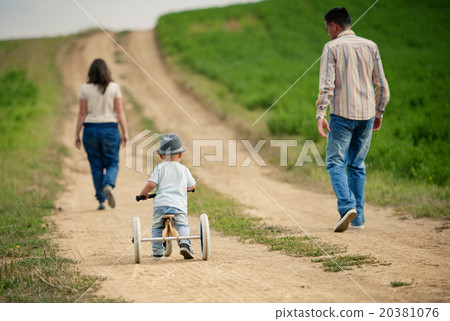Family with little boy on tricycle in nature Family with little boy on tricycle in nature 20381076