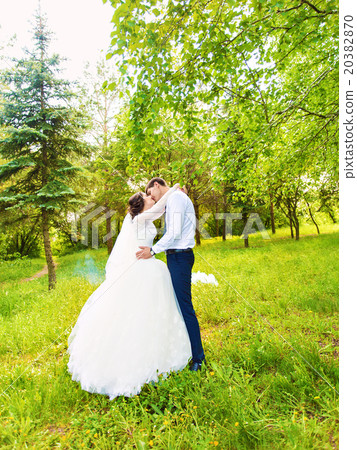 Beautiful wedding couple in park. They kiss and Beautiful wedding couple in park. They kiss and 20382870