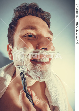 Happy man shaving using razor with cream foam. 20400424