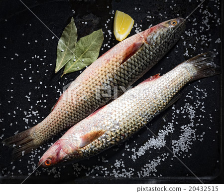 Two raw fish with lemon and salt on a black backgr 20432515