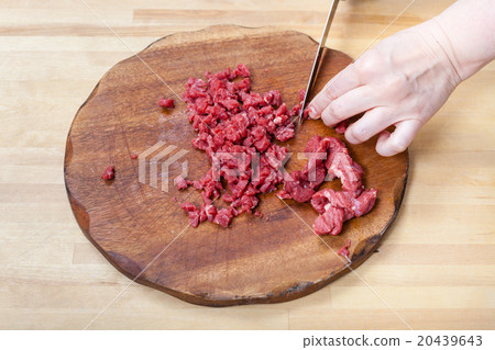 woman cuts meat on wooden cutting board 20439643