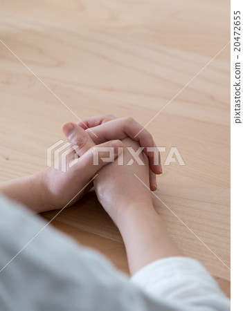 A woman prays, her hands resting on a wooden table, lost in quiet contemplation. A woman prays, her hands resting on a wooden table, lost in quiet contemplation. 20472655