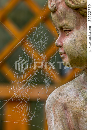 Spider web and stone statue in the garden. 20522779