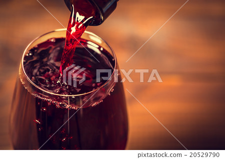 Pouring red wine into the glass against wooden  20529790