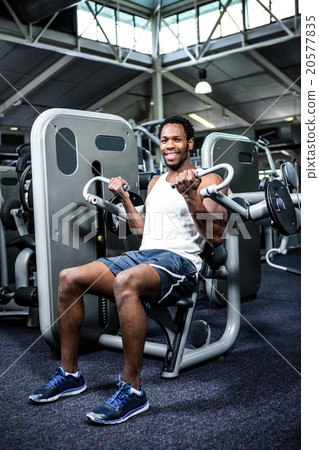 Smiling muscular man using exercise machine 20577835