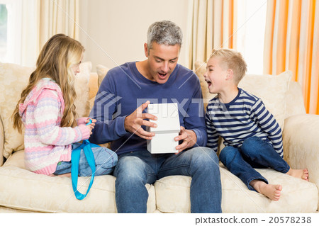 Father opening gift given by children on sofa 20578238