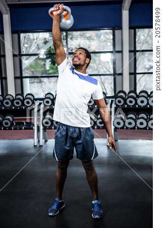 Smiling muscular man lifting kettlebells 20578499