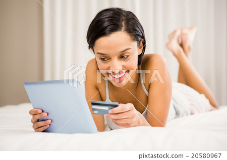 Smiling brunette using tablet and holding credit card Smiling brunette using tablet and holding credit card 20580967