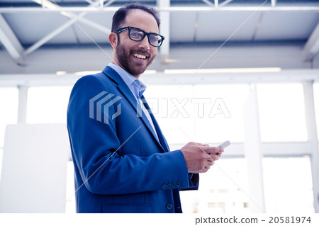 Portrait of happy businessman holding smartphone in office 20581974