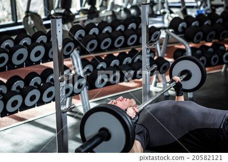 Muscular man lifting barebell while lying on bench 20582121
