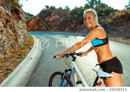 Woman cyclist standing near a bike on a mountain road Woman cyclist standing near a bike on a mountain road 20588553
