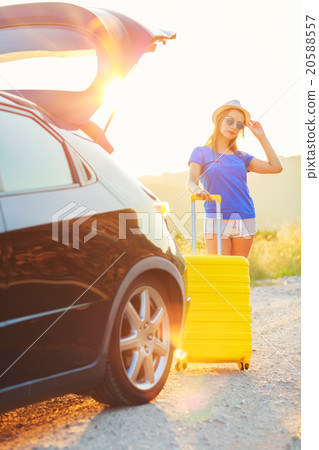 Woman with a yellow suitcase standing near the trunk of a car pa 20588557