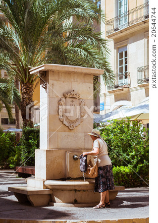 Elderly woman collects water in fountain on street 20644744