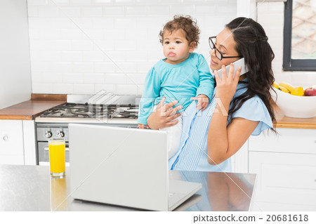Smiling brunette holding her baby and using laptop on phone call 20681618