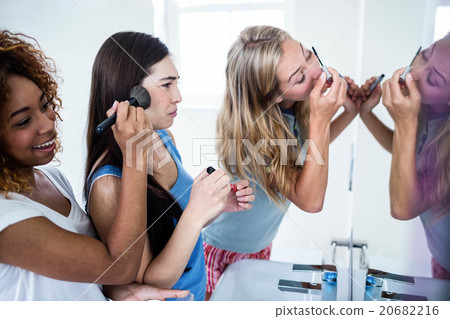 Three smiling friends putting makeup on together Three smiling friends putting makeup on together 20682216